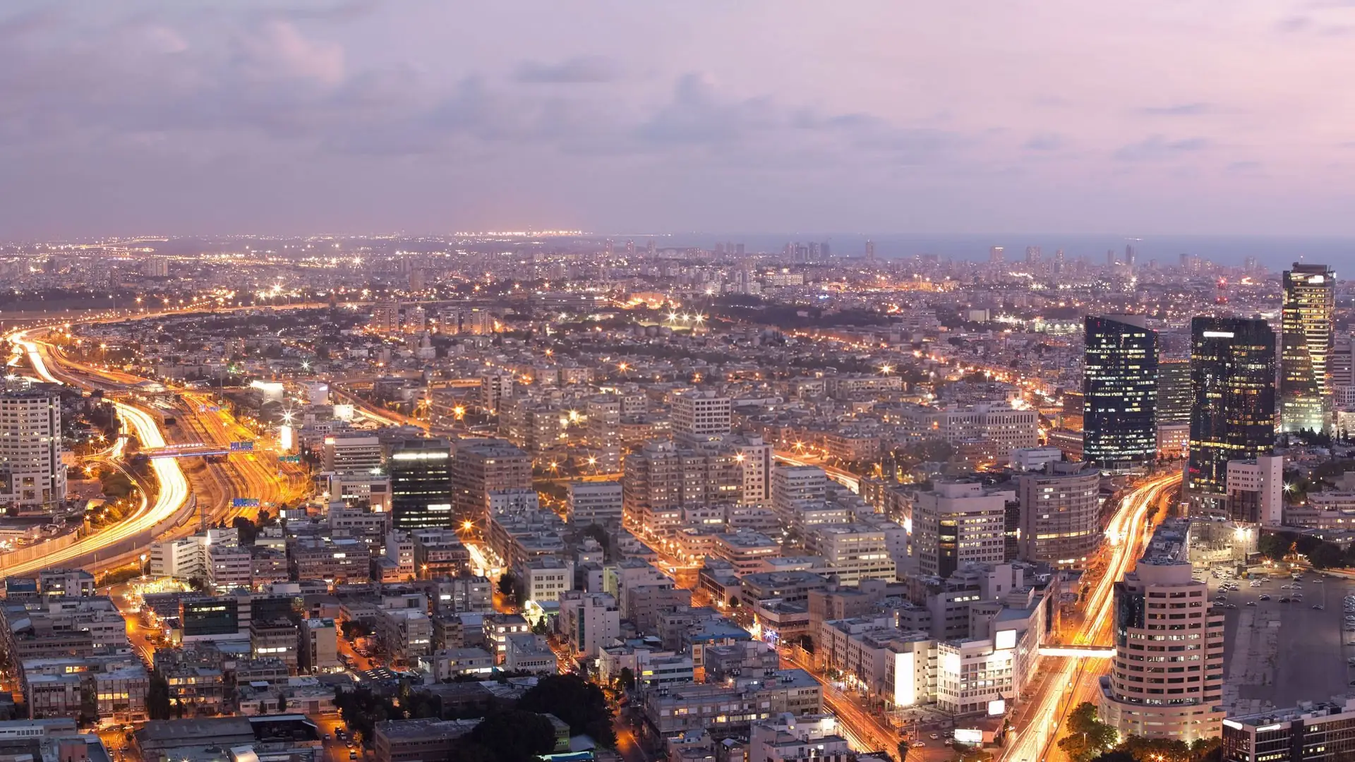 Aerial view of a city skyline at dusk, with highway light trails
